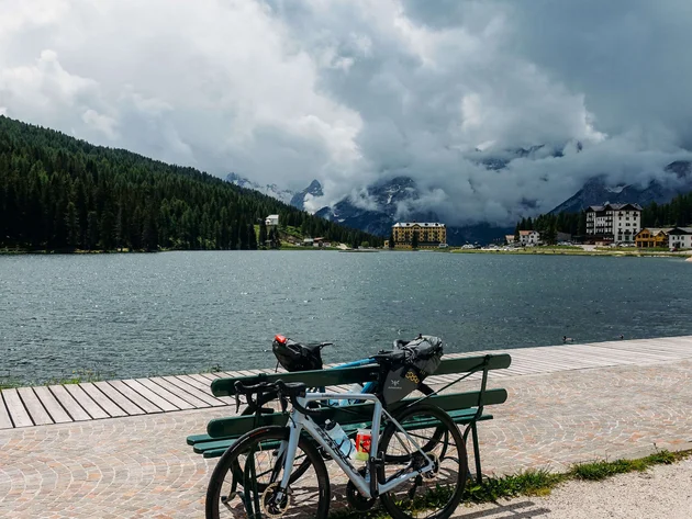 Fahrrad an Bank am See mit bewölkten Bergen im Hintergrund