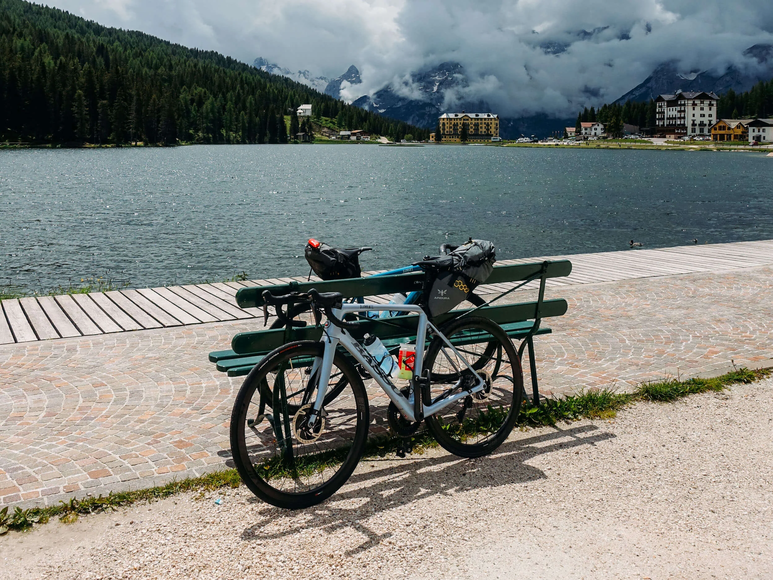 Bikepacking © Hotel Melodia del Bosco Fahrrad an Bank am See mit bewölkten Bergen im Hintergrund