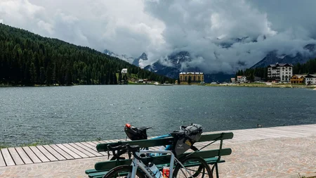 Fahrrad an Bank am See mit bewölkten Bergen im Hintergrund