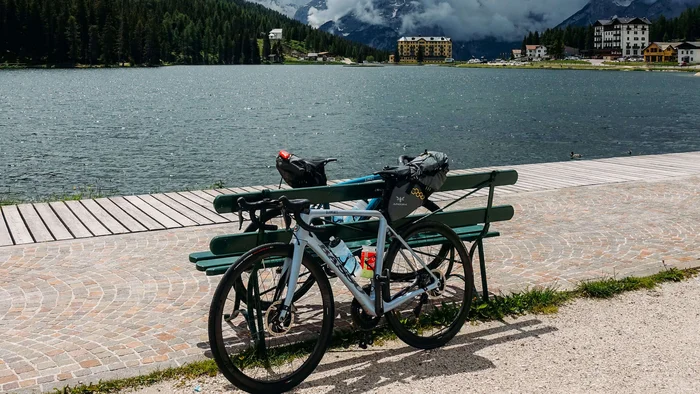 Fahrrad an Bank am See mit bewölkten Bergen im Hintergrund
