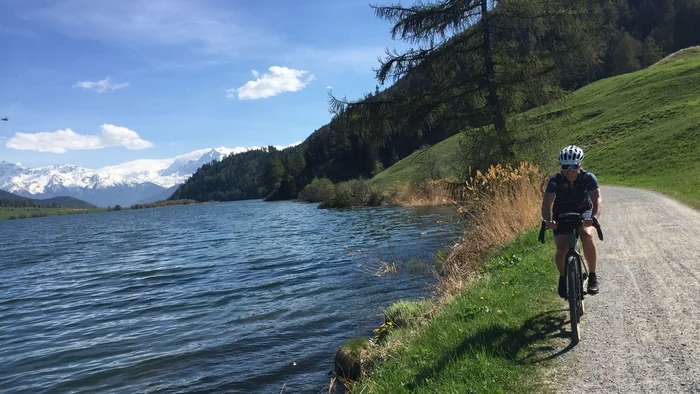Fahrradfahrer auf einem Weg neben See in den Bergen bei sonnigem Wetter
