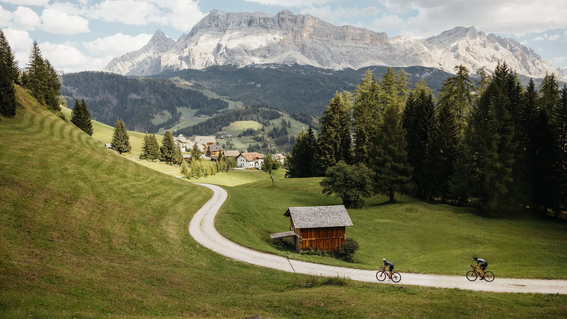 Zwei Radfahrer auf einem Weg im grünen Tal mit Bergen im Hintergrund