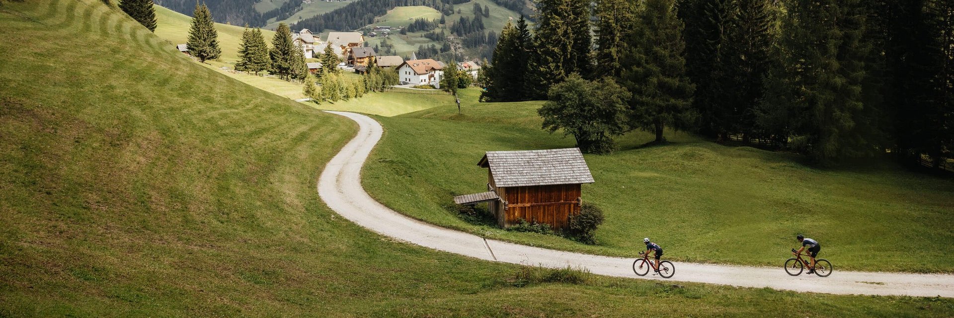 Two cyclists on a path in a green valley with mountains in the background