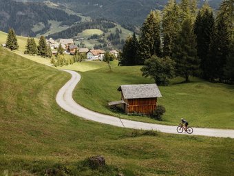 Zwei Radfahrer auf einem Weg im grünen Tal mit Bergen im Hintergrund