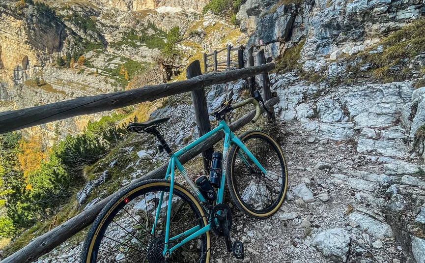 Fahrrad auf felsigem Bergweg mit Bergpanorama und Holzzaun
