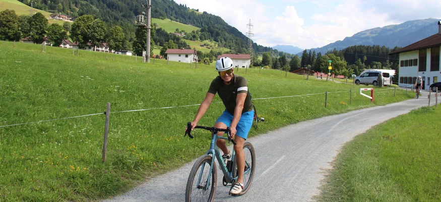Radfahrer auf Landstraße vor grünen Hügeln und Bergen