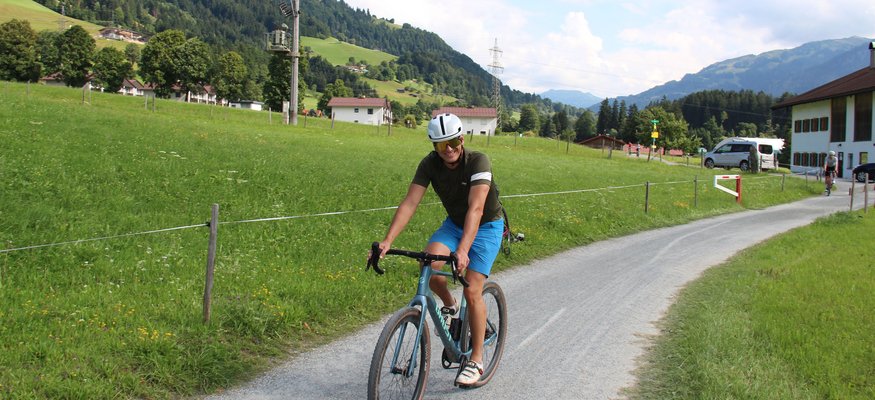 Radfahrer auf Landstraße vor grünen Hügeln und Bergen