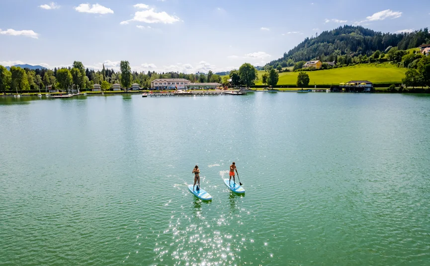 Zwei Personen paddleboarden auf einem See bei sonnigem Wetter
