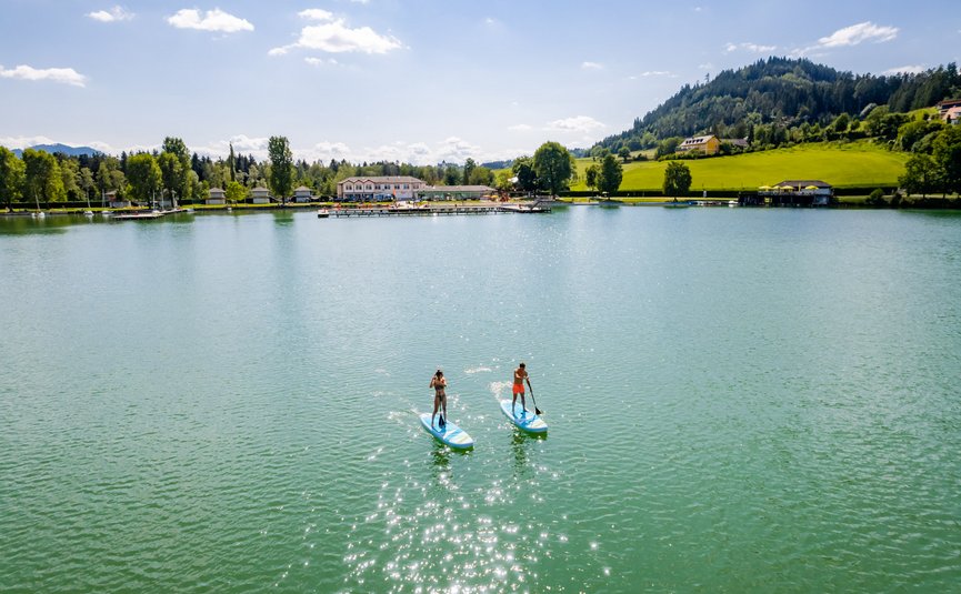 Zwei Personen paddleboarden auf einem See bei sonnigem Wetter
