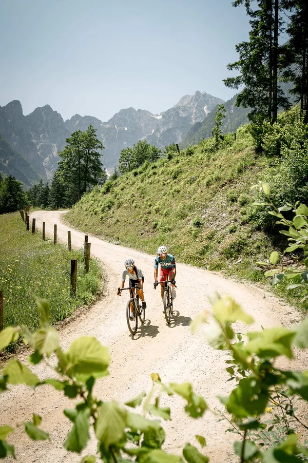 Slovenia Gravel Experience © Alain Rumpf Zwei Radfahrer auf einem Bergweg mit Bergen im Hintergrund