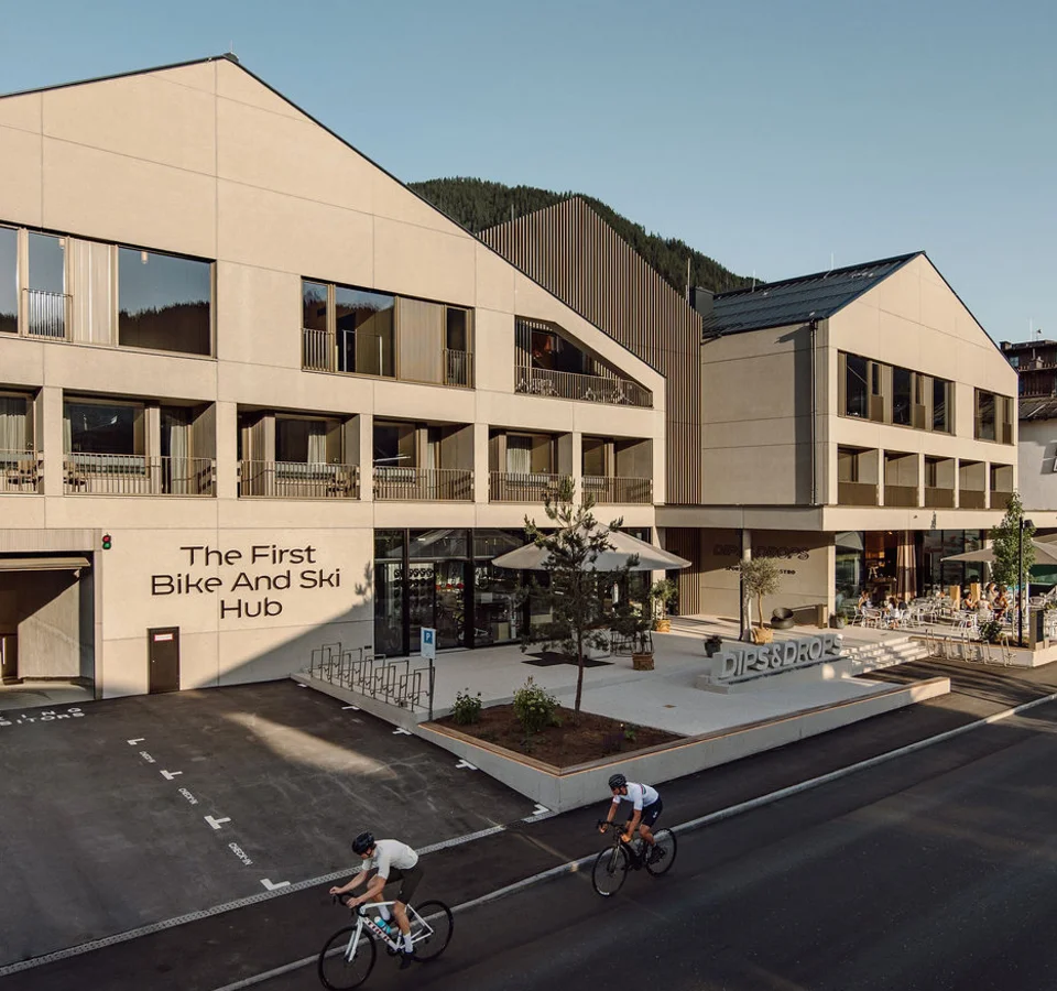 Zwei Radfahrer vor modernem Gebäude mit Schriftzug The First Bike And Ski Hub