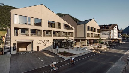 Zwei Radfahrer vor modernem Gebäude mit Schriftzug The First Bike And Ski Hub