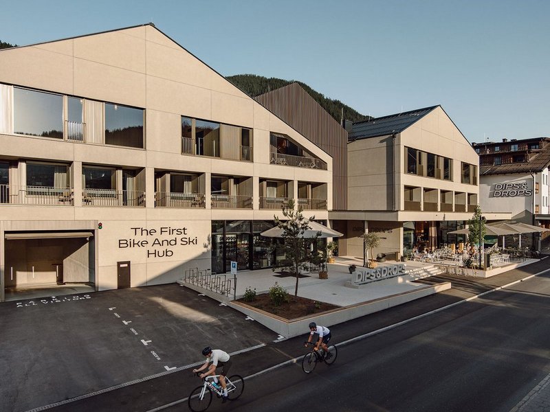 Zwei Radfahrer vor modernem Gebäude mit Schriftzug The First Bike And Ski Hub