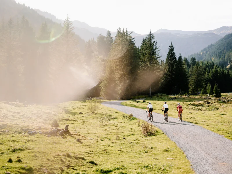 Gravelbike Holidays © Saalbach.com - Moritz Ablinger Drei Radfahrer auf einem Weg in einer Berglandschaft mit Nadelbäumen