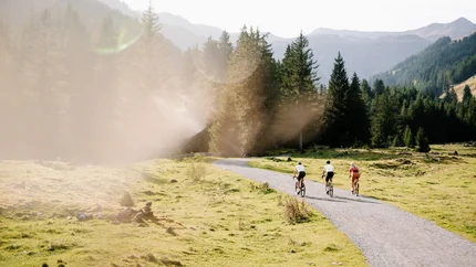 Three cyclists riding on a path in a mountainous forested area