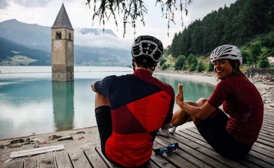 Zwei Radfahrer am See neben einem versunkenen Kirchturm sitzen und Eis essen