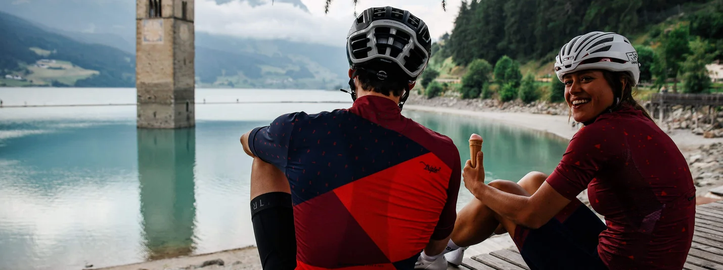 View of Lake Reschen © Felix Saller Two cyclists sitting by a lake with a submerged church tower enjoying ice cream