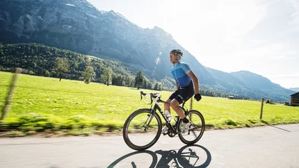 Mann fährt Mountainbike auf Bergstraße bei sonnigem Wetter