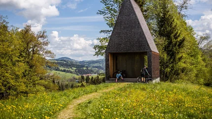 Cyclists at modern wooden pavilion in blooming meadow landscape