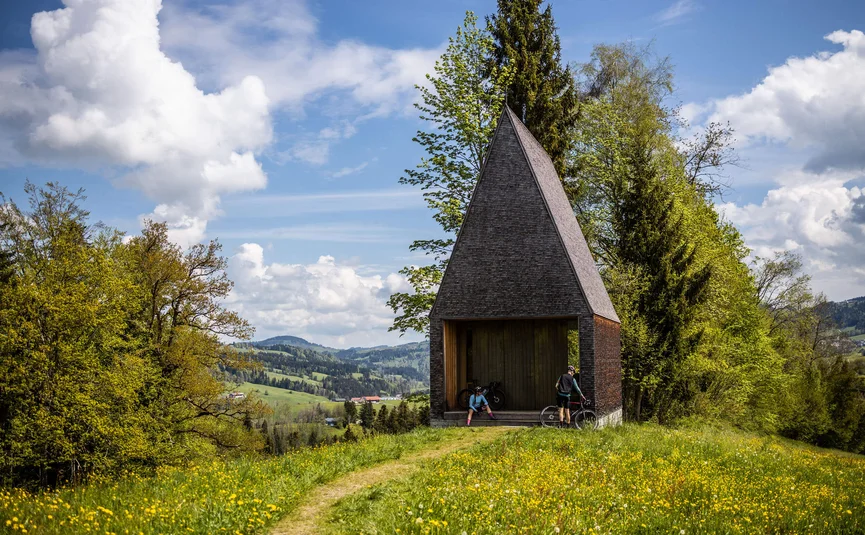 Cyclists at modern wooden pavilion in blooming meadow landscape
