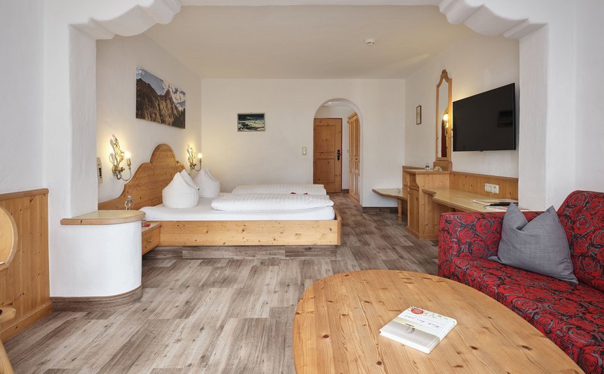 Gemütliches Hotelzimmer mit Doppelbett, rotem Sofa und Holzmöbeln