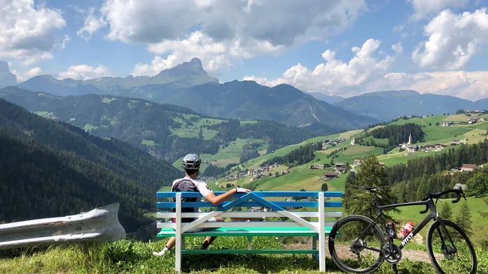Radfahrer auf Bank blickt auf grüne Berge und Dorf im Tal