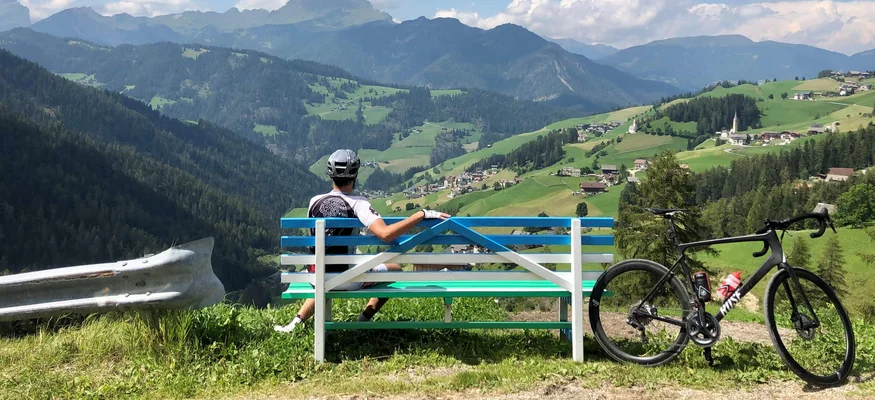 Radfahrer auf Bank blickt auf grüne Berge und Dorf im Tal