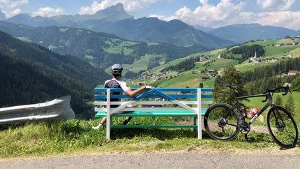 Radfahrer auf Bank blickt auf grüne Berge und Dorf im Tal