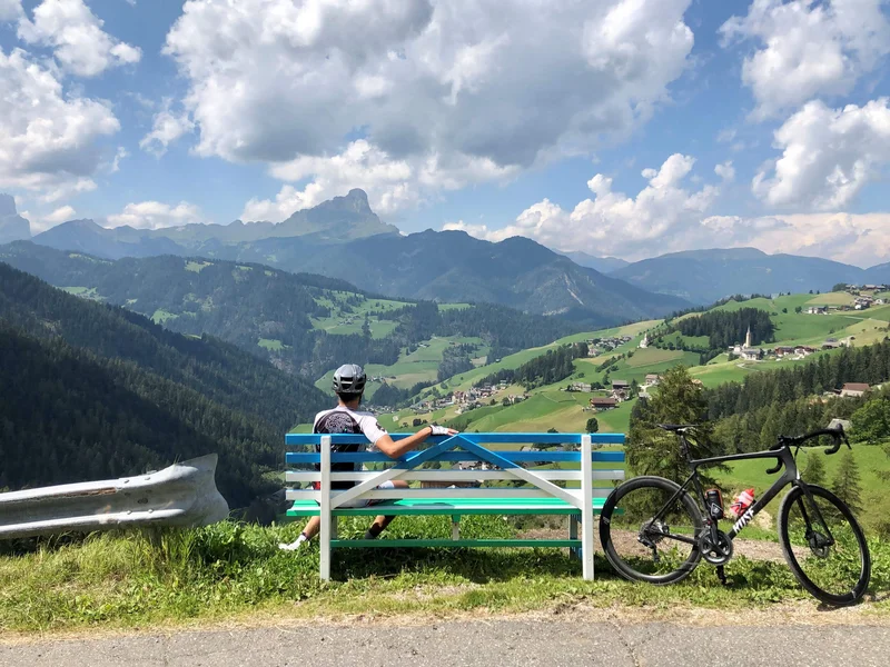 Radfahrer auf Bank blickt auf grüne Berge und Dorf im Tal