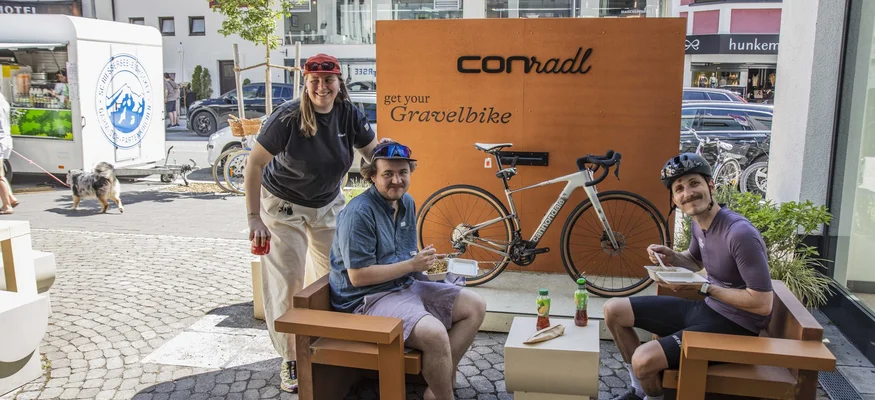 Das war das Ride ’n Gravel Testival 2026! © Sport Conrad-Leon Hoesch Drei Personen vor einem Gravelbike-Schild sitzen und essen in einer Stadt