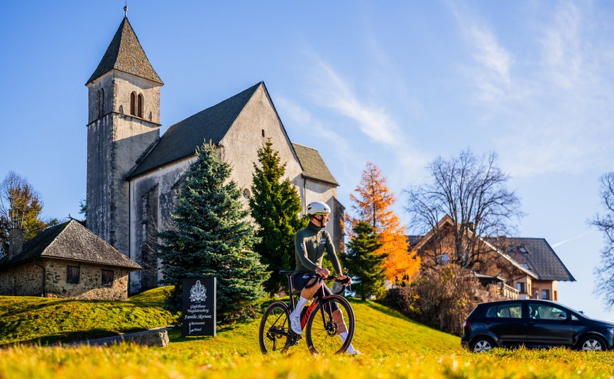 Cyclist in front of church and colorful autumn trees on sunny day