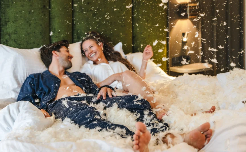 Couple laughing on bed during a feather pillow fight