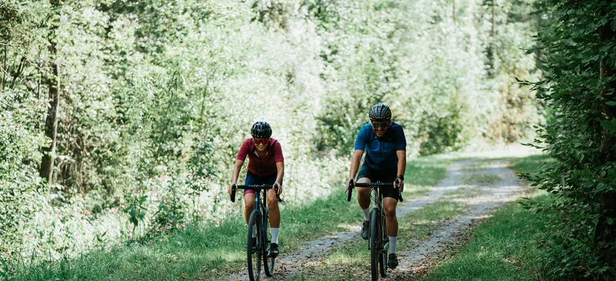 Graveln für Anfänger © Moritz Hübner Zwei Radfahrer fahren auf einem Waldweg entlang grüner Bäume.