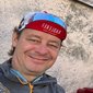Man wearing cycling cap smiling with a drink on table by textured wall