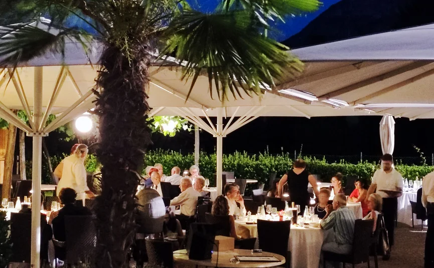Anderen beim Abendessen im Außenrestaurant unter beleuchteten Sonnenschirmen zuschauen