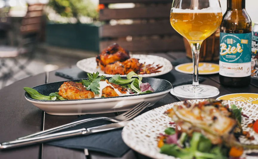Teller mit Hähnchen, Salat und ein Glas Bier auf einem Tisch im Freien