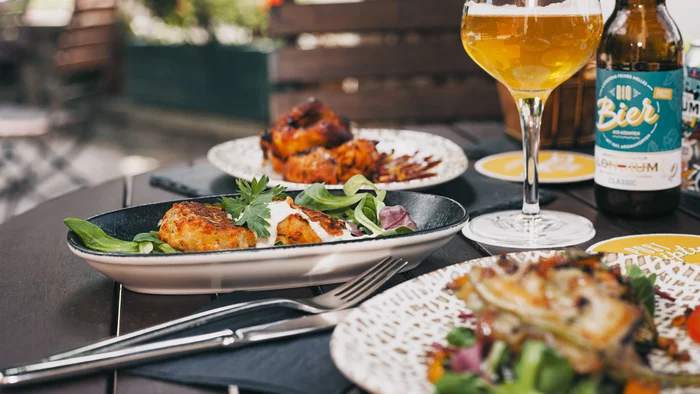 Teller mit Hähnchen, Salat und ein Glas Bier auf einem Tisch im Freien