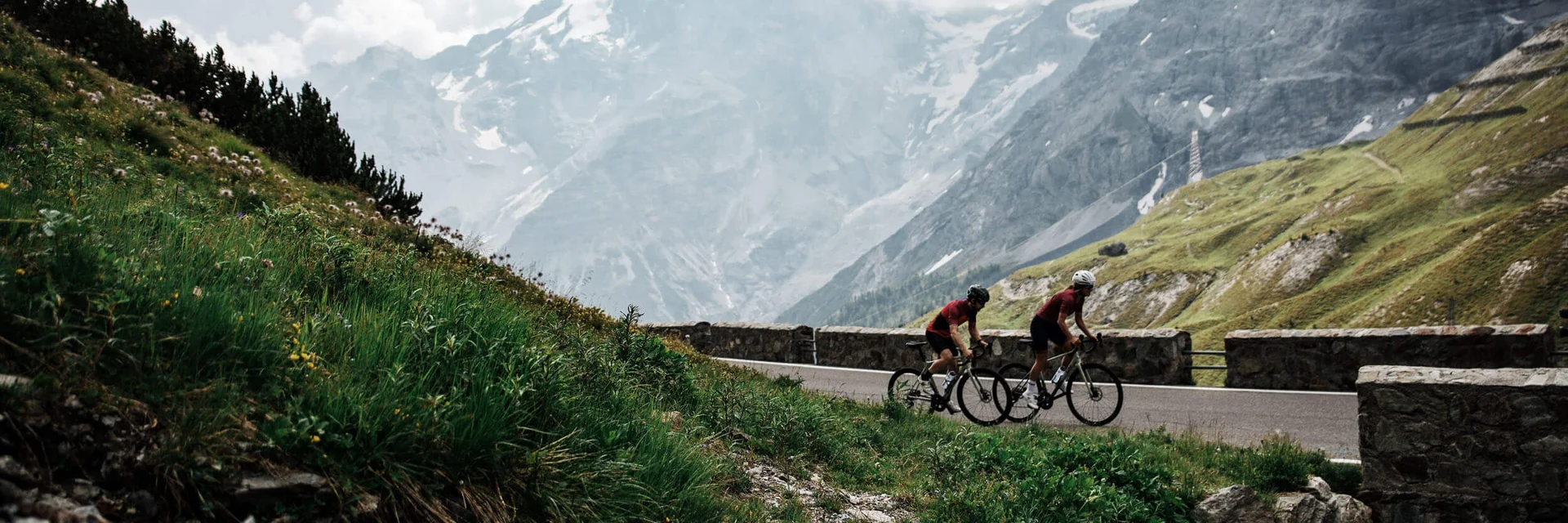 Zwei Radfahrer fahren auf Bergstraße mit schneebedeckten Bergen im Hintergrund