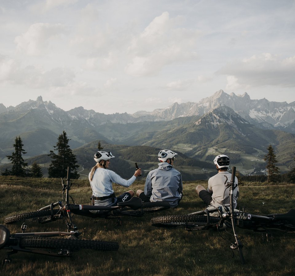 Drei Radfahrer sitzen auf einer Wiese mit Mountainbikes vor Berglandschaft