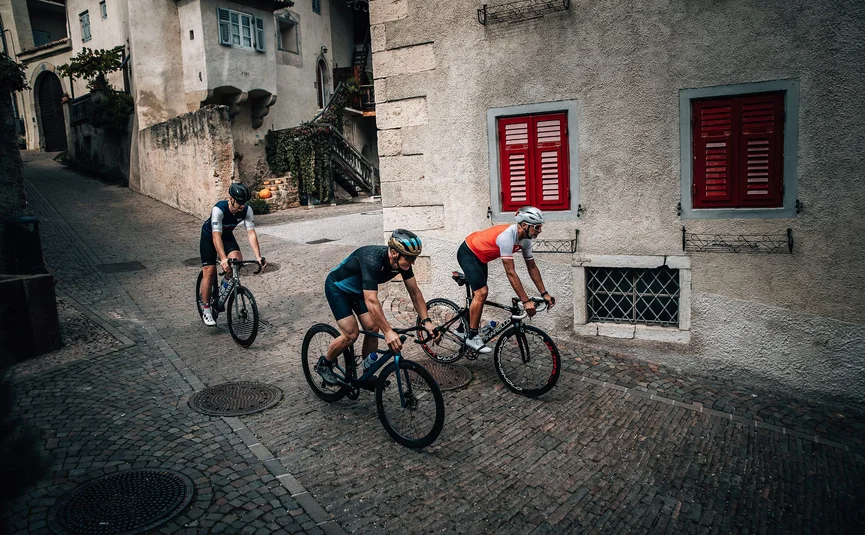 Drei Radfahrer fahren auf gepflasterter Straße in historischem Dorf
