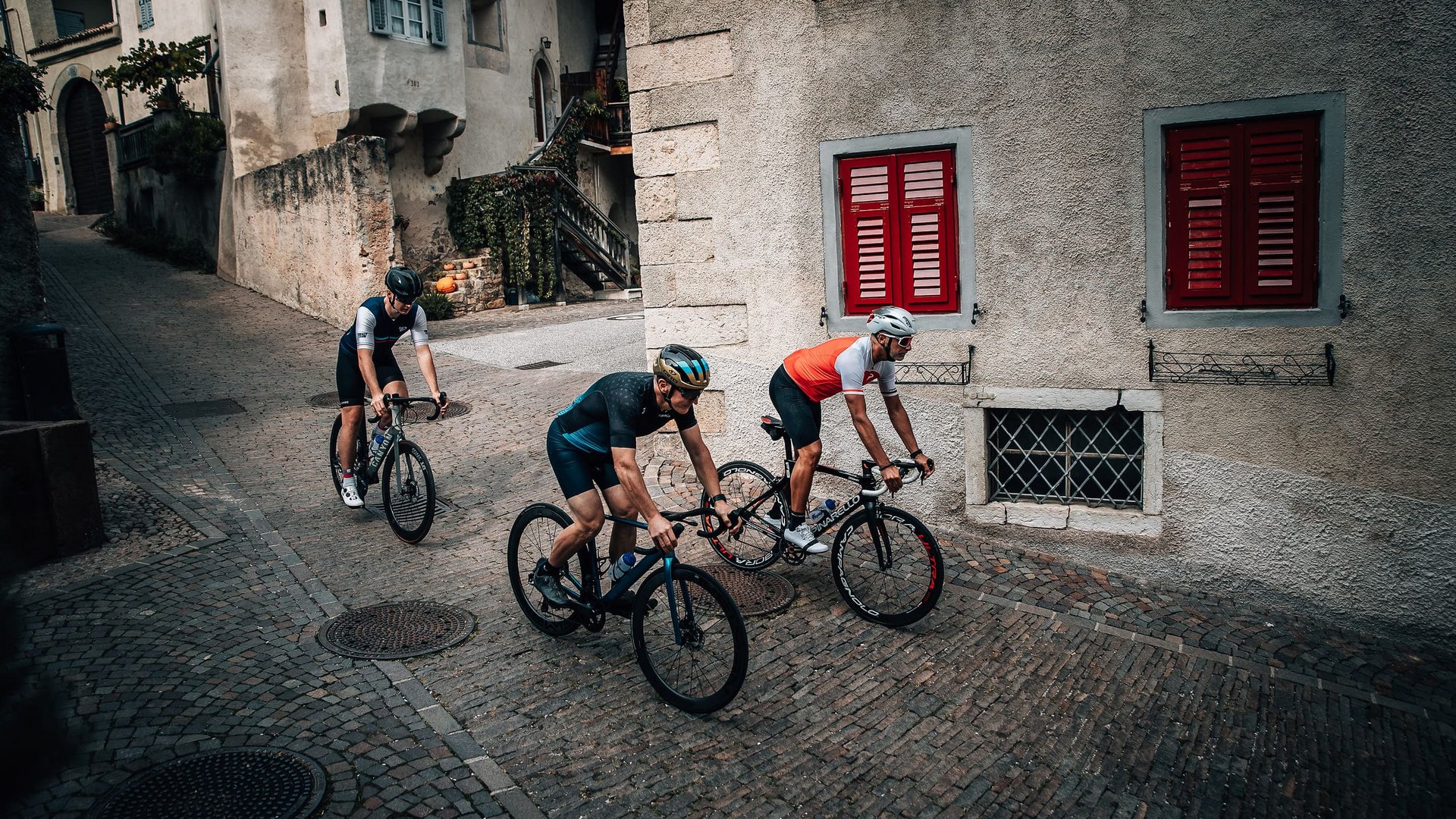 Drei Radfahrer fahren auf gepflasterter Straße in historischem Dorf