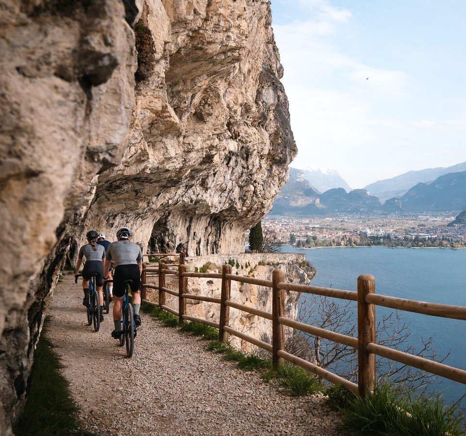 Radfahrer auf einem Pfad entlang einer Felswand mit Seeblick