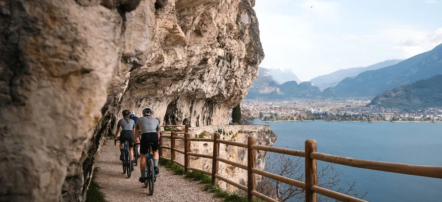 Radfahrer auf einem Pfad entlang einer Felswand mit Seeblick