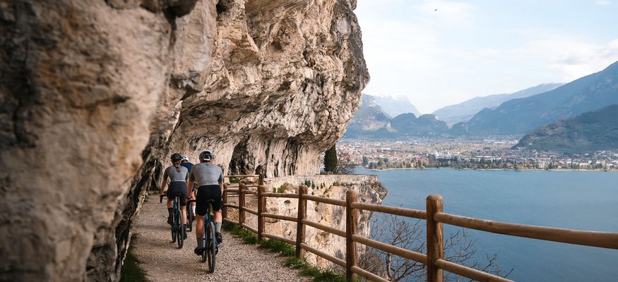 Radfahrer auf einem Pfad entlang einer Felswand mit Seeblick