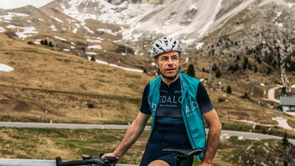 Rennradfahrer mit Helm vor Berglandschaft mit wenig Schnee