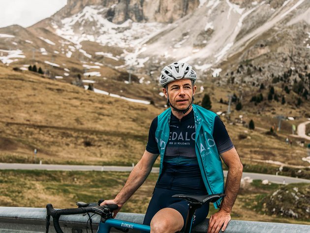 Alpine Gravel Experience © Chiara Redaschi Rennradfahrer mit Helm vor Berglandschaft mit wenig Schnee