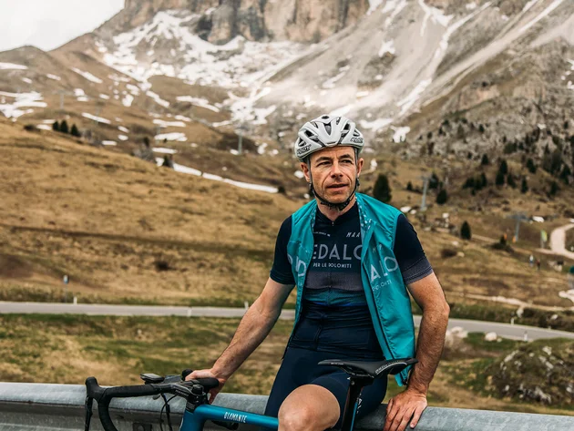 Cyclist wearing helmet resting with bike in mountainous landscape with patches of snow