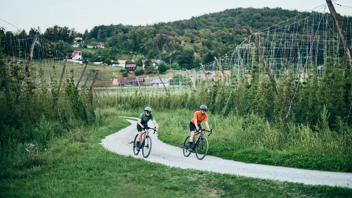 Two cyclists riding on a gravel path in a green rural landscape.