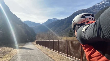 Bikepacking von Wien nach Athen © Jan Koller Radfahrer auf Bergstraße mit Zaun und Bergen im Hintergrund bei sonnigem Wetter
