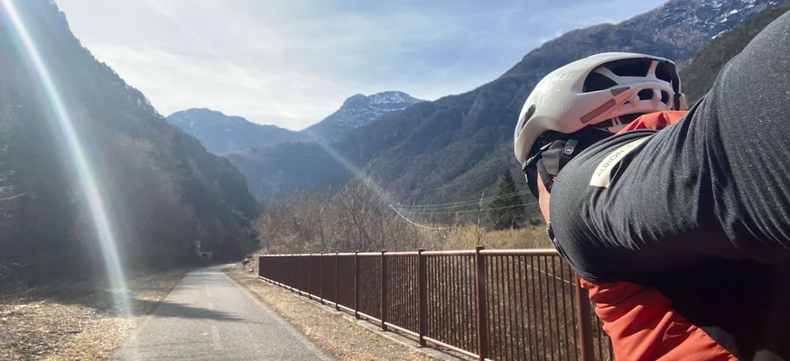 Bikepacking von Wien nach Athen © Jan Koller Radfahrer auf Bergstraße mit Zaun und Bergen im Hintergrund bei sonnigem Wetter